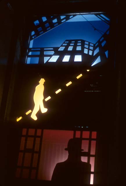 An abstracted image of an urban subject. The top third of the image is devoted to a multi-story building, with the lights on in the ground floor windows, against a darkening blue sky. The middle third features a yellow glowing figure walking diagonally across the scene following a dashed yellow line, and the bottom third shows a black silhouetted figure standing in front of a dark red background framed in a lattice grid.